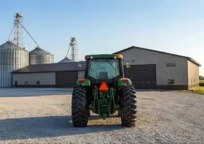 Tractor in front of a steel building and silos on a farm.